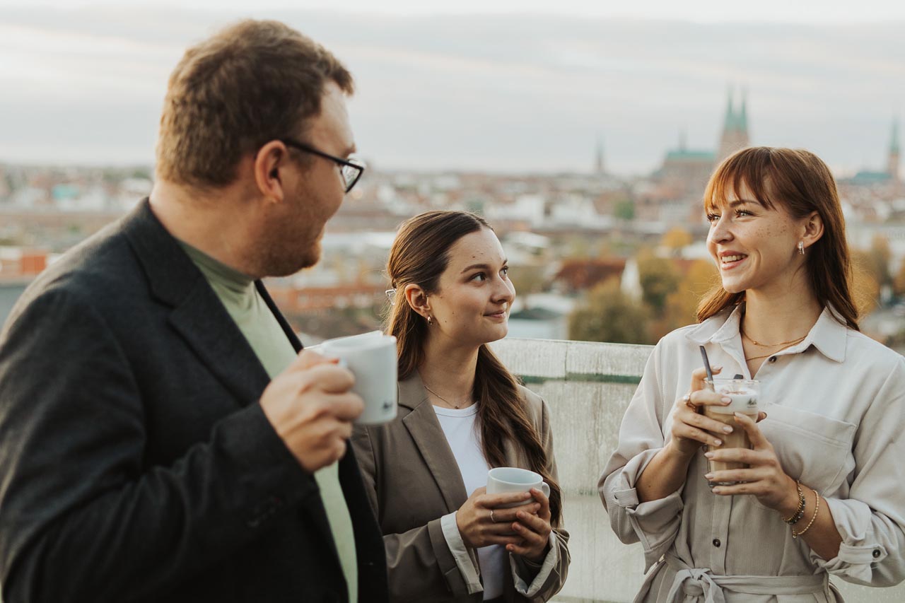 Drei Personen stehen auf der Dachterasse in der Sonne mit Blick über Lübeck